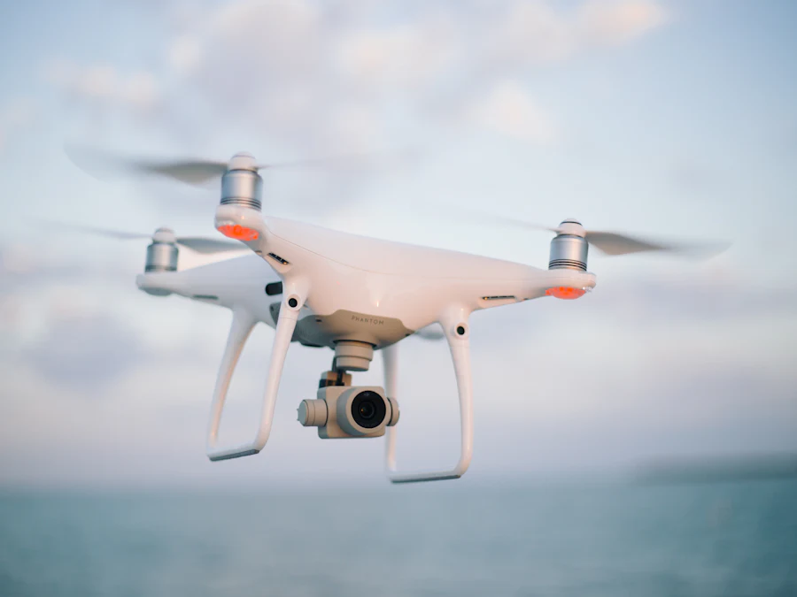 White quadcopter drone with a camera gimbal in flight against a bright, partly cloudy sky