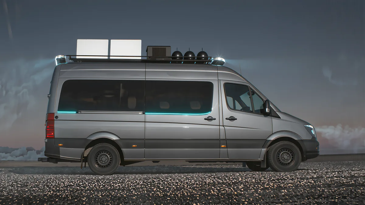Side view of the parked command van at dusk with two flat satellite panels on the roof and the roof light bars switched on